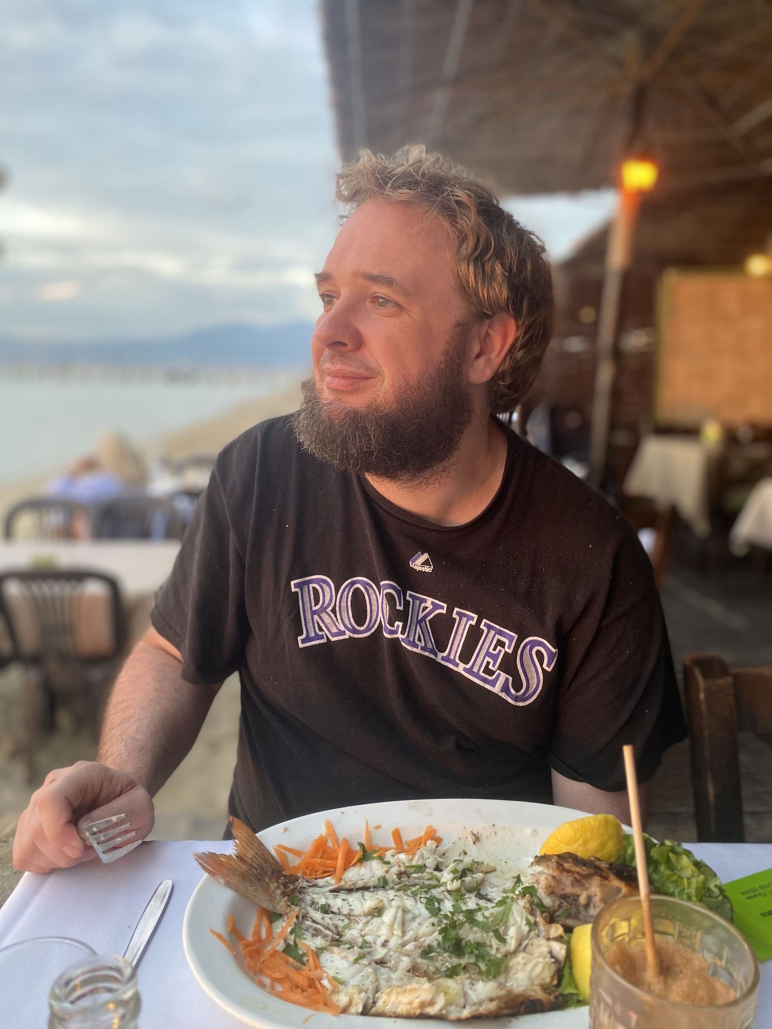 Someone in a Colorado Rockies shirt enjoying a seafood meal with sauce at an outdoor restaurant patio.