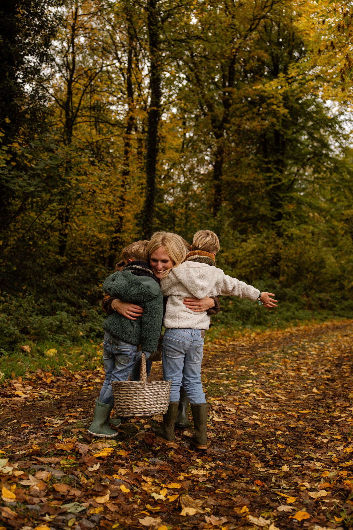 Three children share a warm group hug on a leaf-covered autumn forest path.