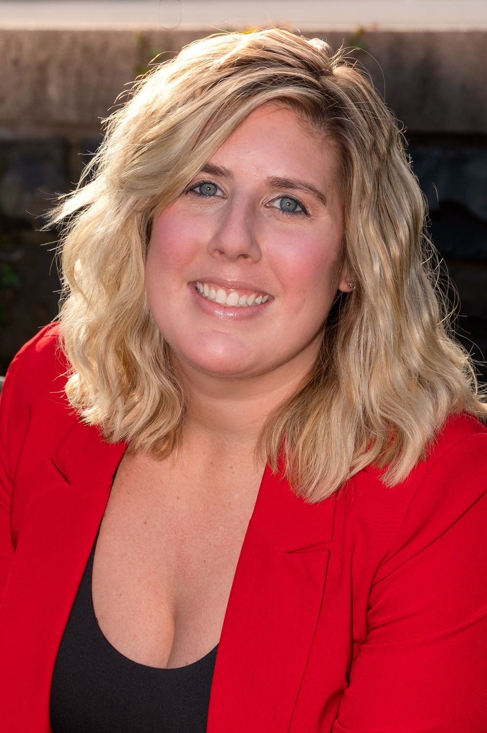 Professional headshots of a person in red blazer and black top against outdoor setting.