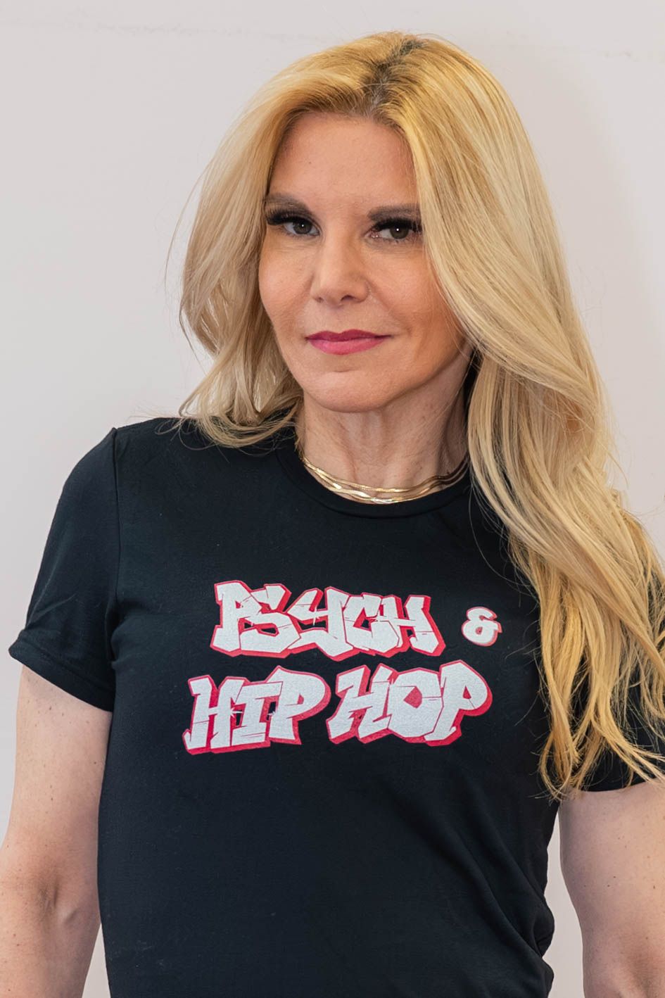 Blonde woman wearing black hip hop t-shirt with red and white graffiti style text against white background.