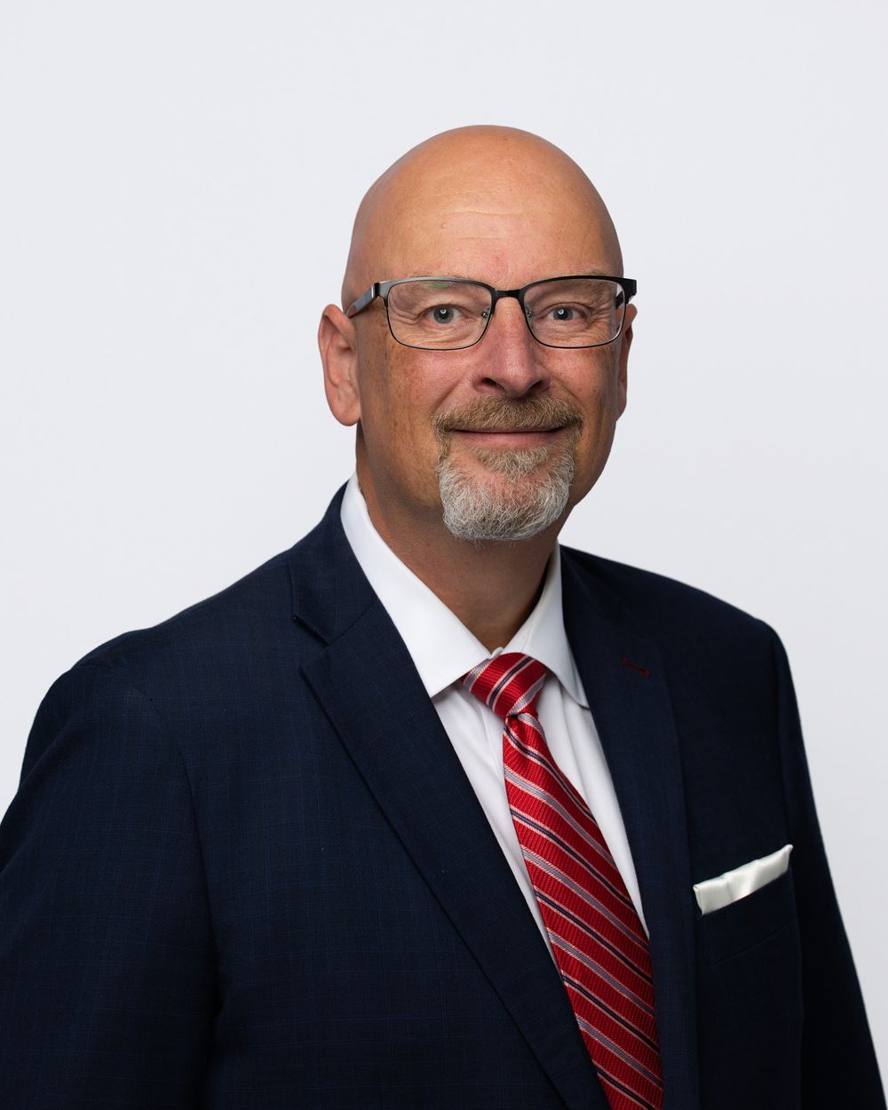 Professional headshot of someone in a dark suit and red striped tie against a light background.