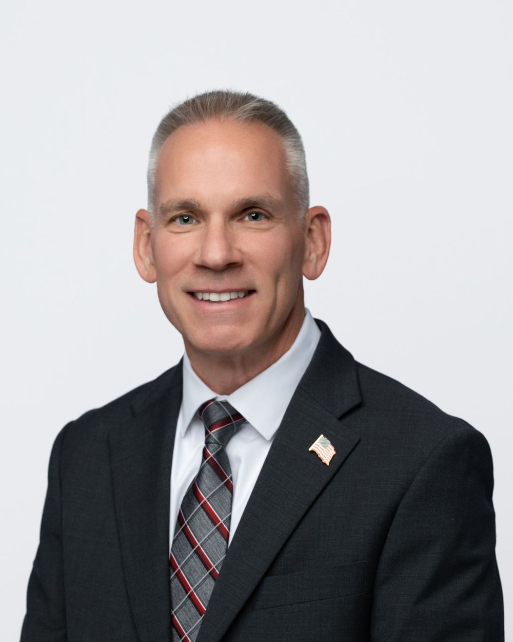 Professional headshot series of a person in a black suit and plaid tie against white background.
