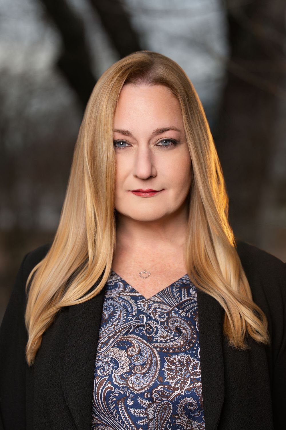 Professional headshots of a person wearing a black blazer and patterned blouse against dark background.