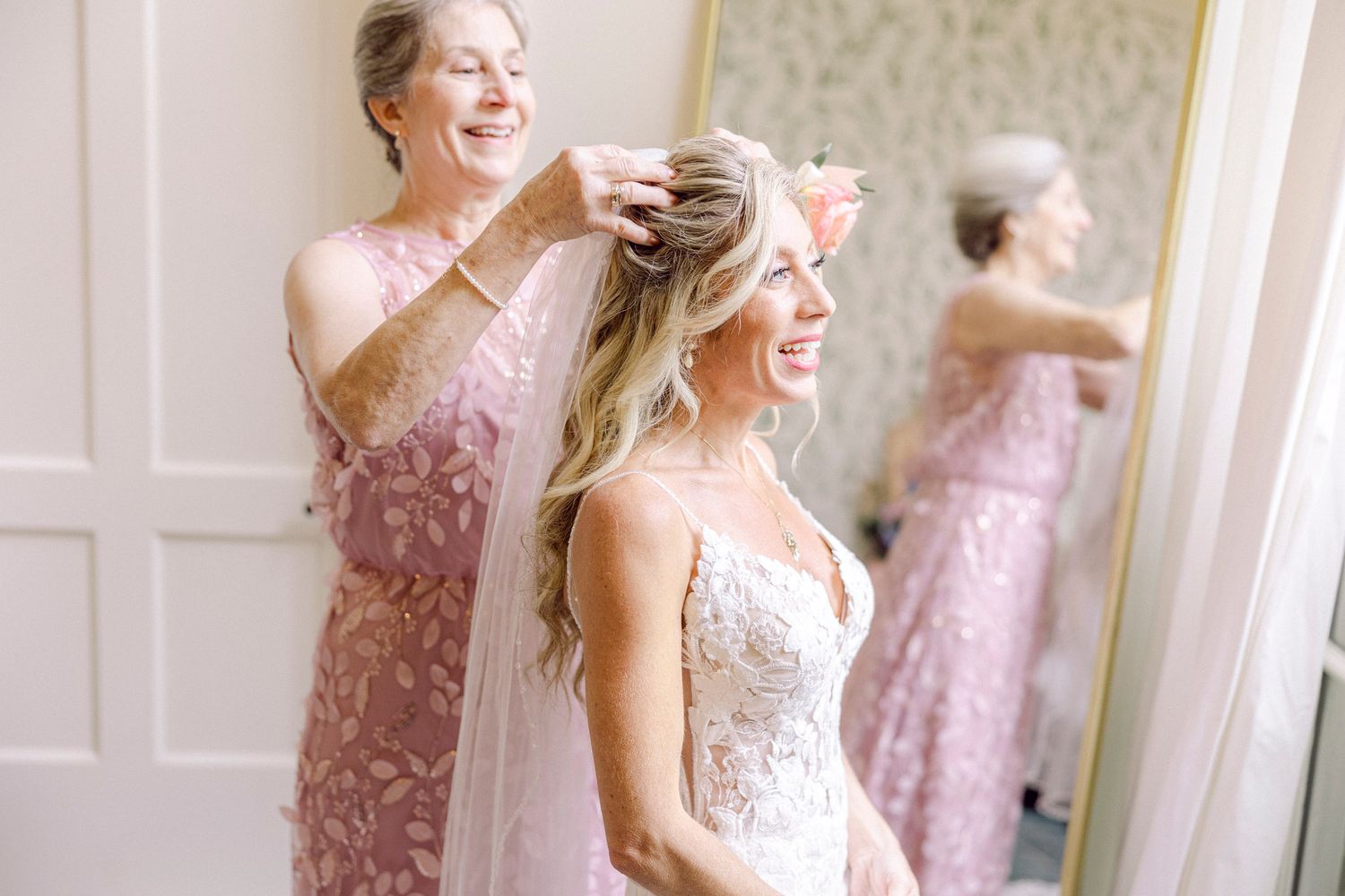 Wedding party wearing pink and white dresses laughs together in a bright indoor setting.