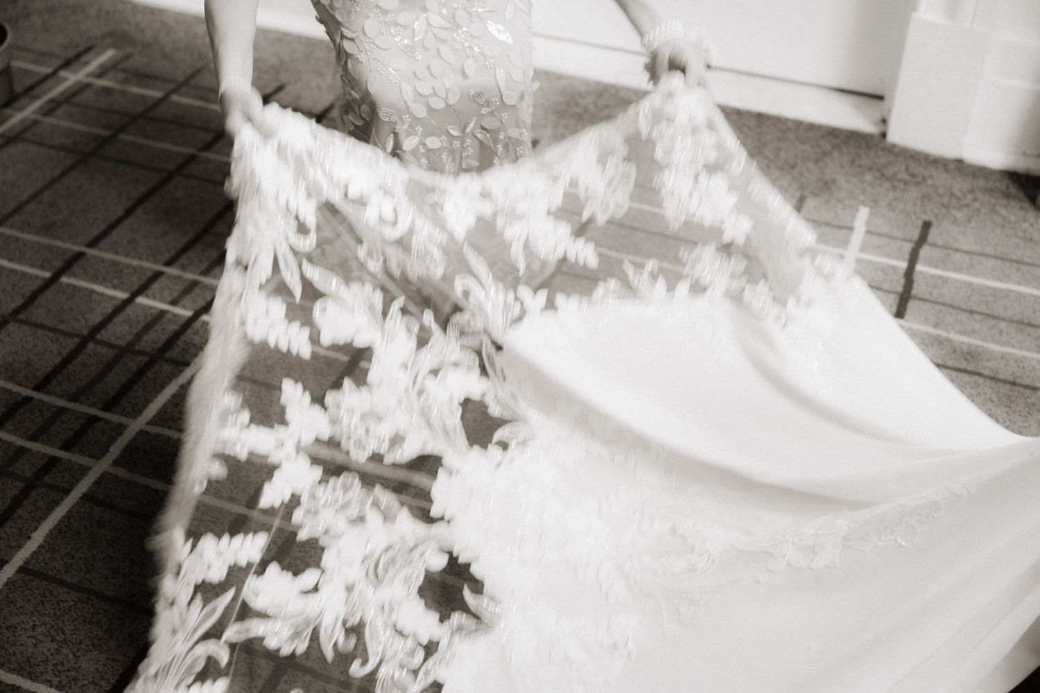 A white wedding dress with floral lace details hangs elegantly against a light background.