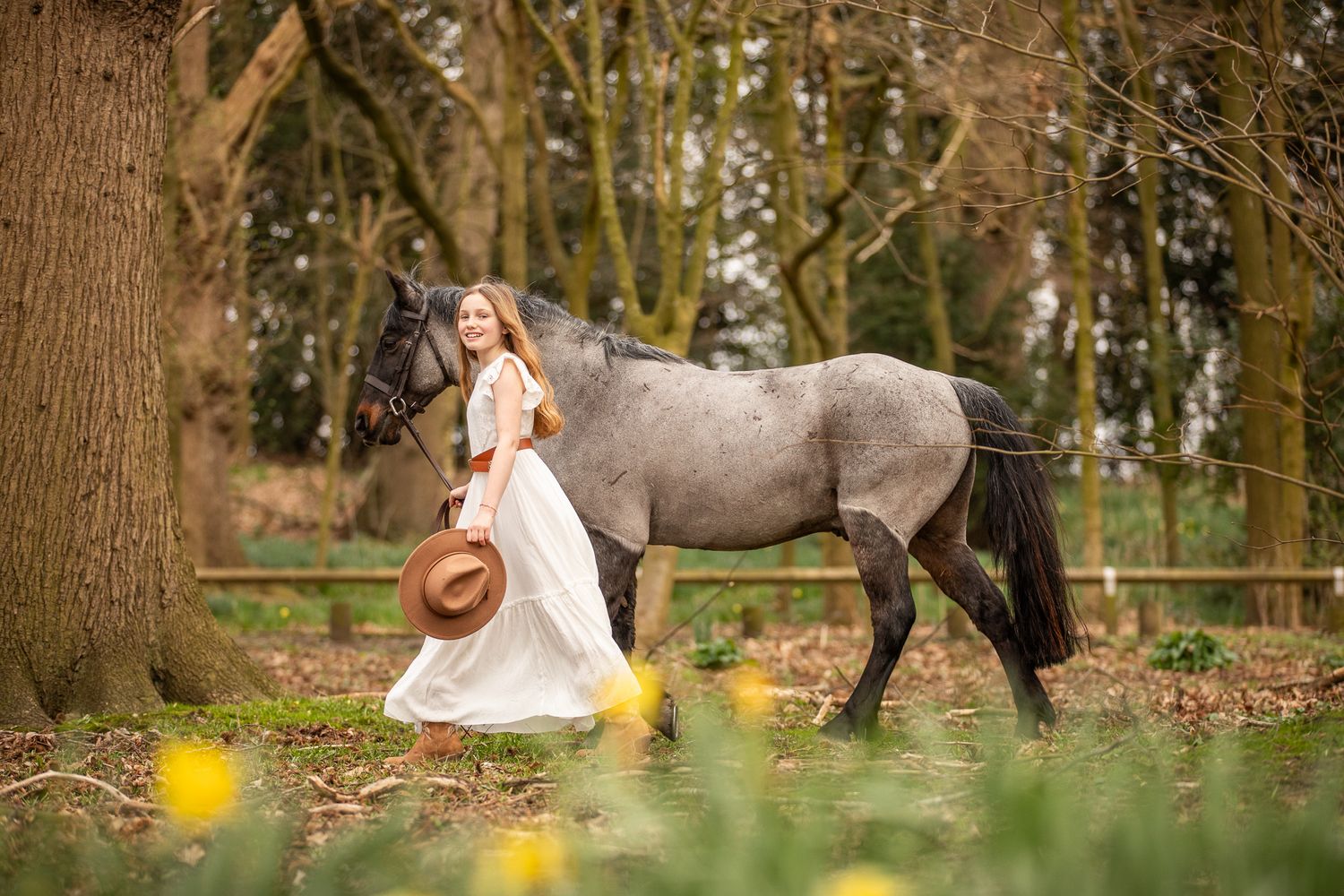 A couple in wedding attire walks together through a scenic wooded area with daffodils in the foreground.