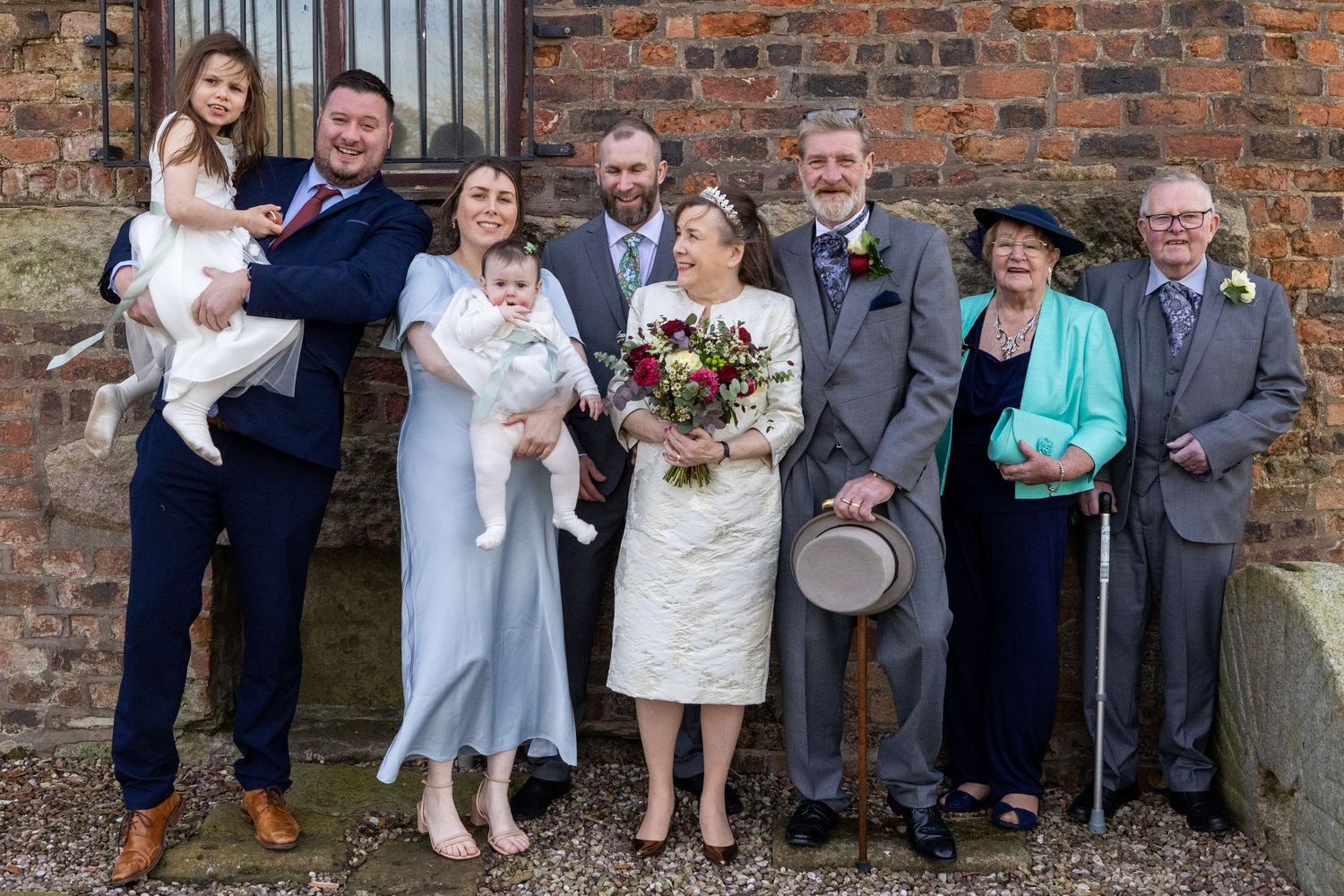 All the family gathered for relaxed wedding group photo outside against the brick wall at Windmill Farm, Burscough.