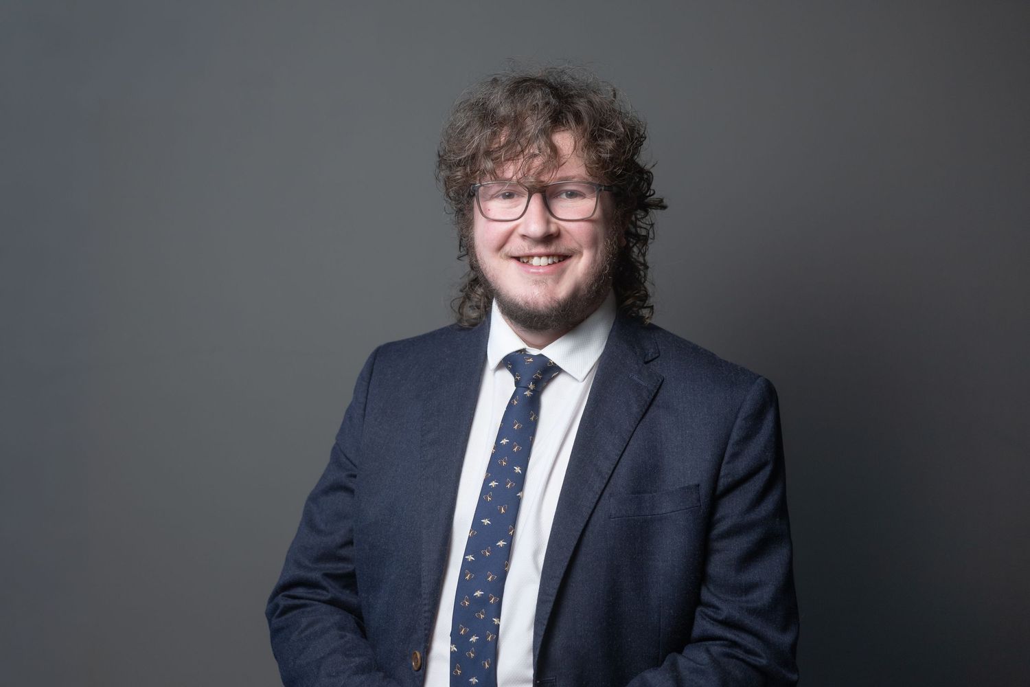 Professional headshot of James wearing a navy suit and tie.