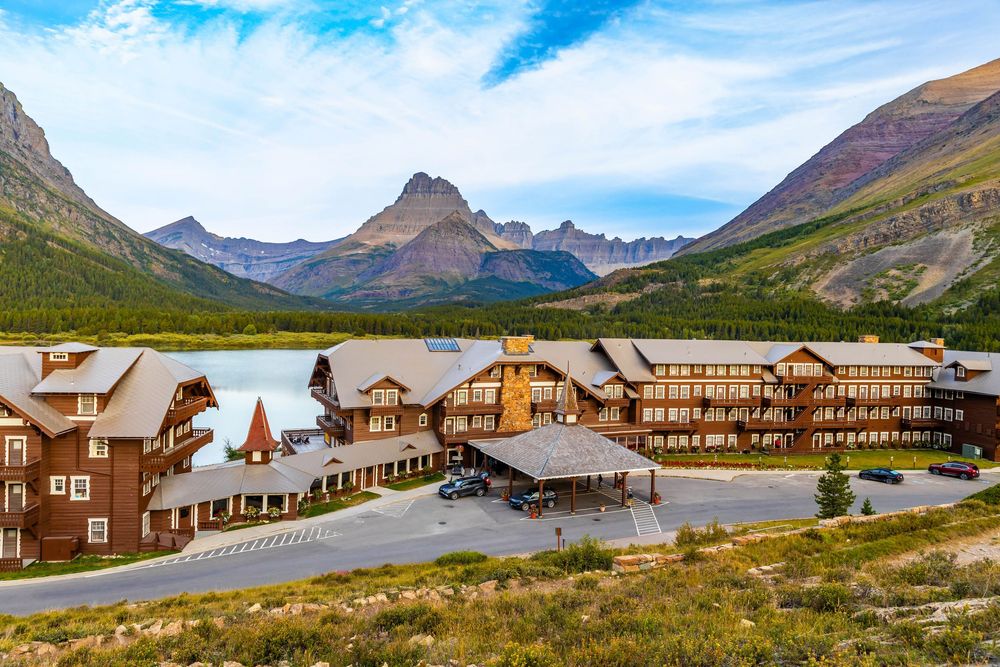 A panoramic view of the Many Glacier Hotel nestled against majestic mountain peaks in a scenic wilderness setting.