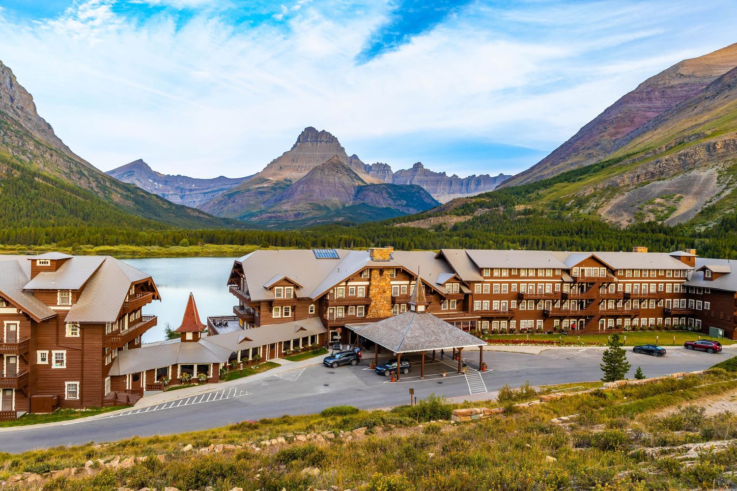 A panoramic view of the Many Glacier Hotel nestled against majestic mountain peaks in a scenic wilderness setting.
