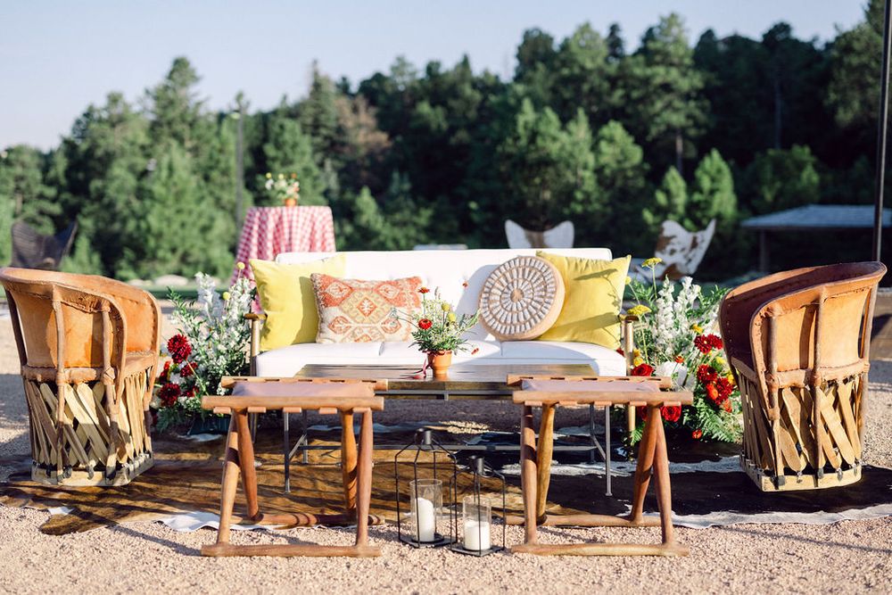 Outdoor wedding reception setup with wooden tables and chairs arranged in a row under white umbrellas in a garden setting.