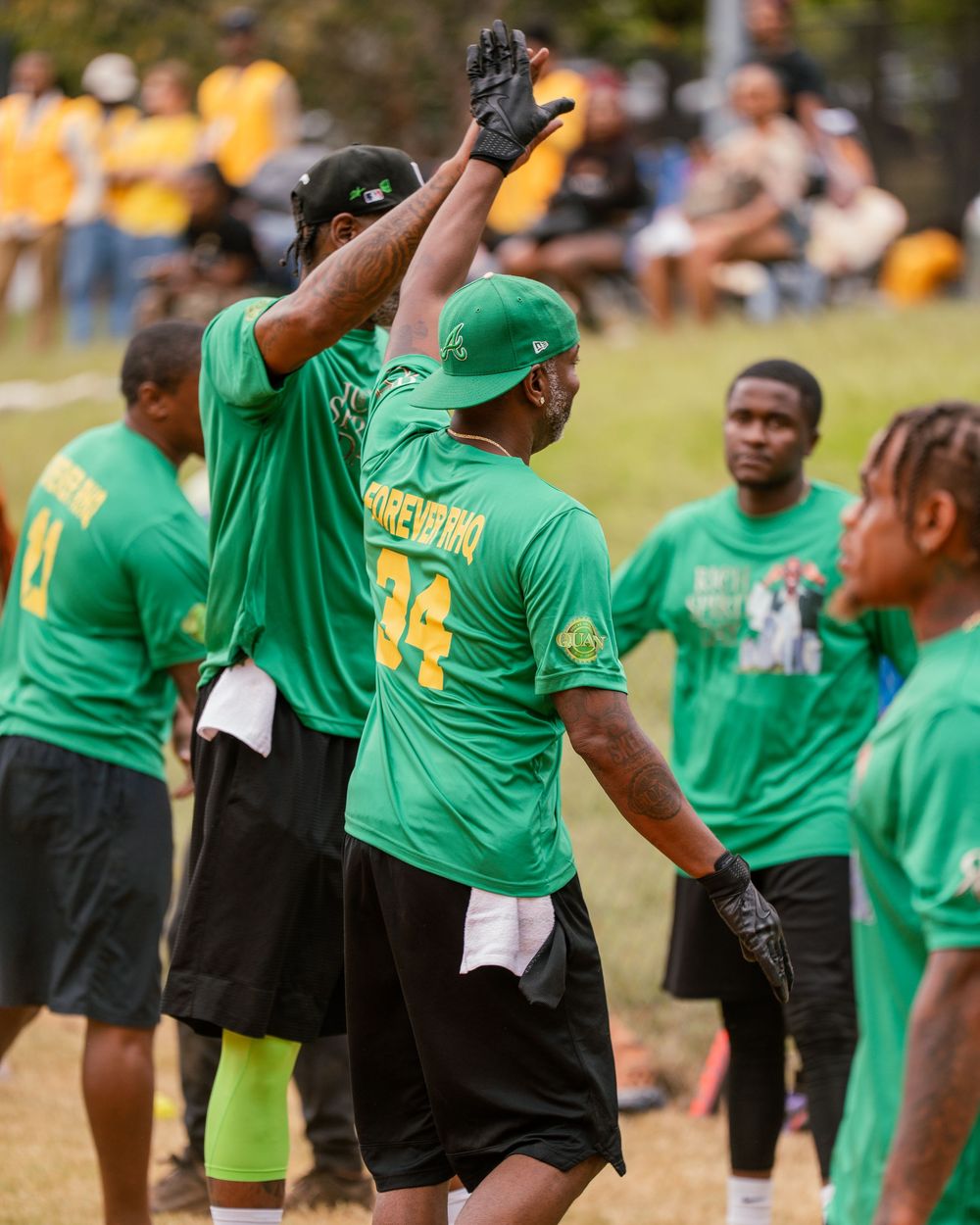 A group of players in green jerseys celebrate together on a sports field during a sunny day.