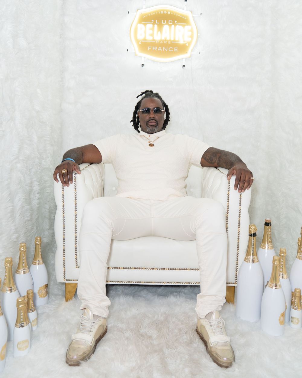 Person in all-white outfit sits on white couch with multiple white decorative bottles arranged in front.