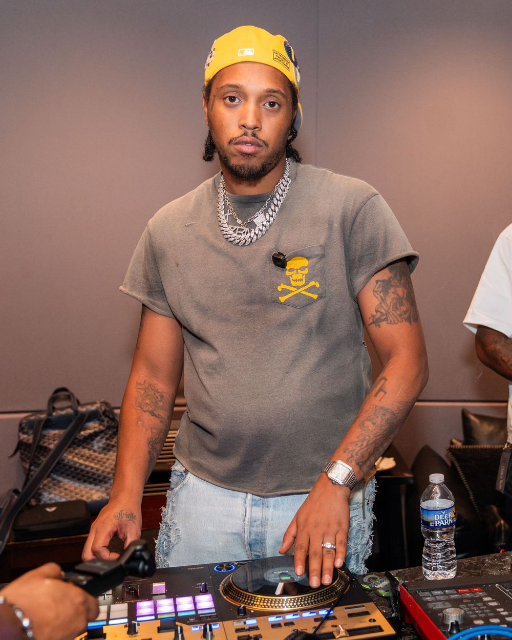 DJ wearing yellow cap and grey shirt performs on professional mixing equipment at music event.