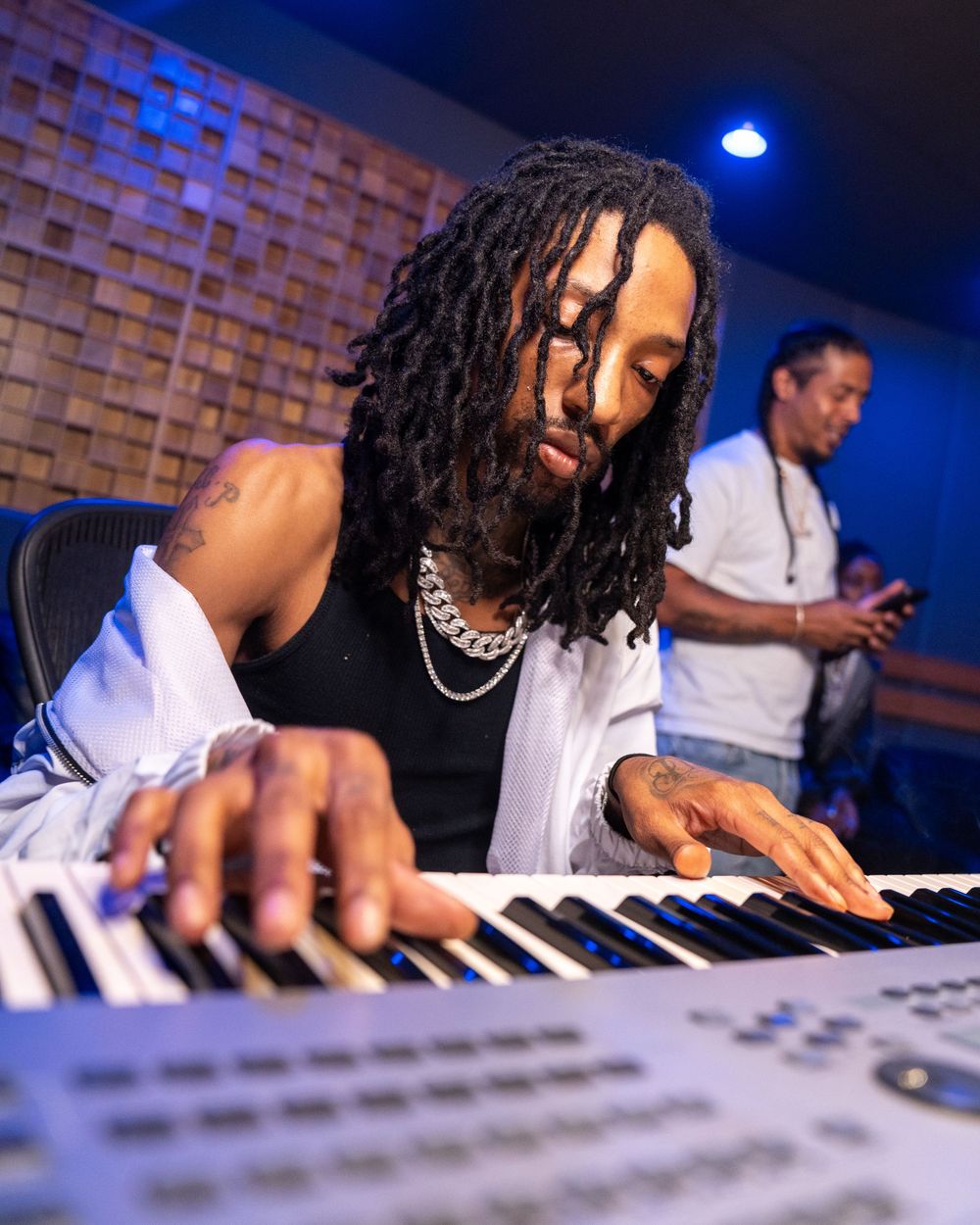 A musician plays on a mixing console and keyboard in a recording studio with blue lighting.