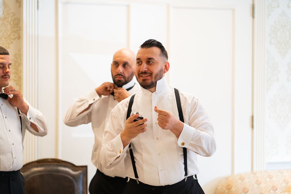 Three people in formal attire stand together looking at mobile phones in a bright white room.
