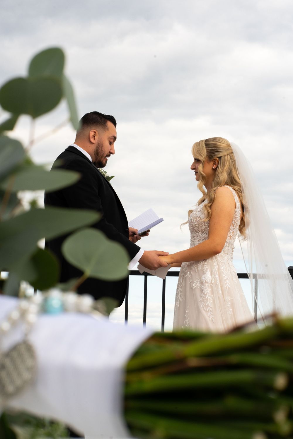 A bride and groom share an intimate moment during their outdoor wedding ceremony against a cloudy sky.