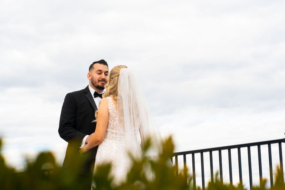 Newlywed couple shares a romantic kiss on a balcony overlooking a scenic landscape at sunset.