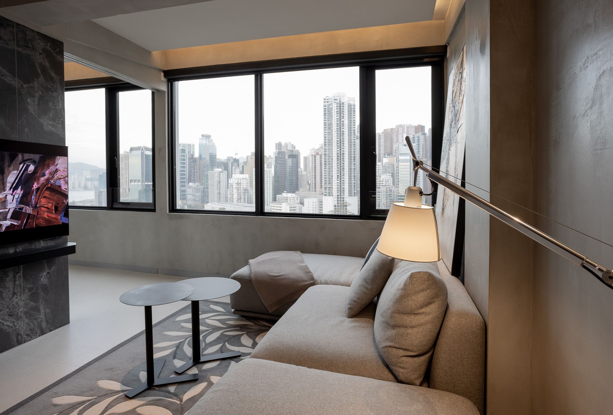 Contemporary living room with floor-to-ceiling windows overlooking city skyline and grey sofa.