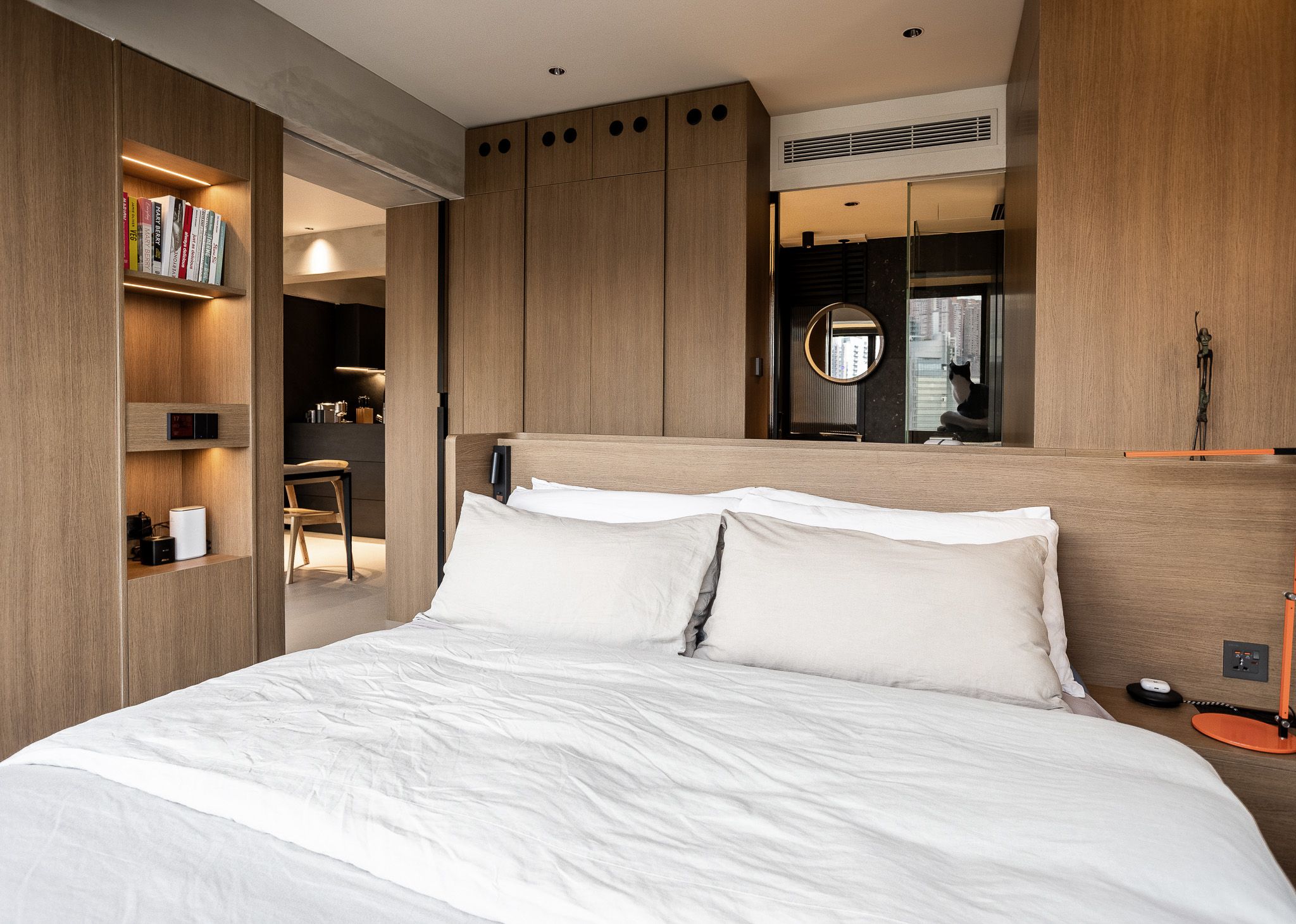 Minimalist bedroom with white bedding, warm wood built-in wardrobes, open shelving, and integrated storage design.