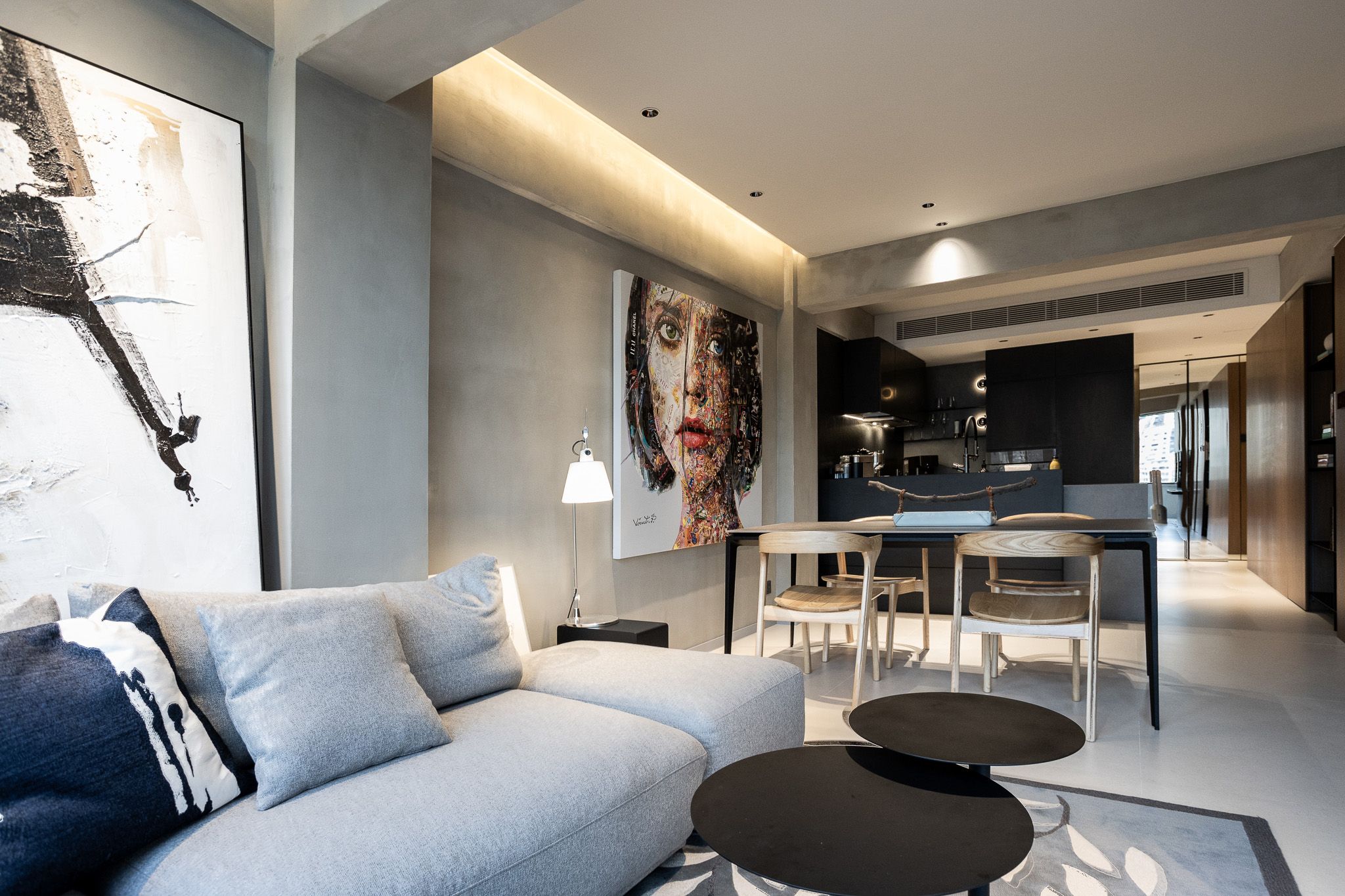 Bright modern living room with grey sofa, abstract wall art, black coffee tables, and open-plan dining area.
