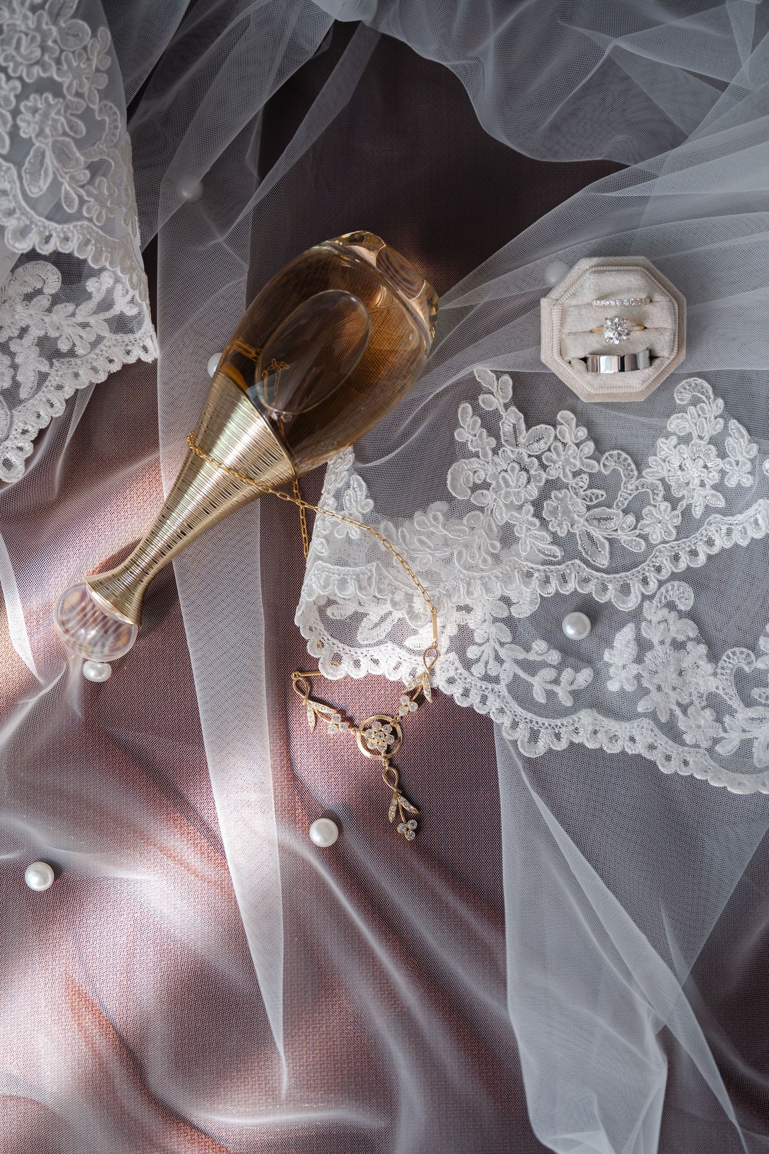 Delicate white lace and tulle fabric details with champagne colored glass creating an elegant bridal composition.