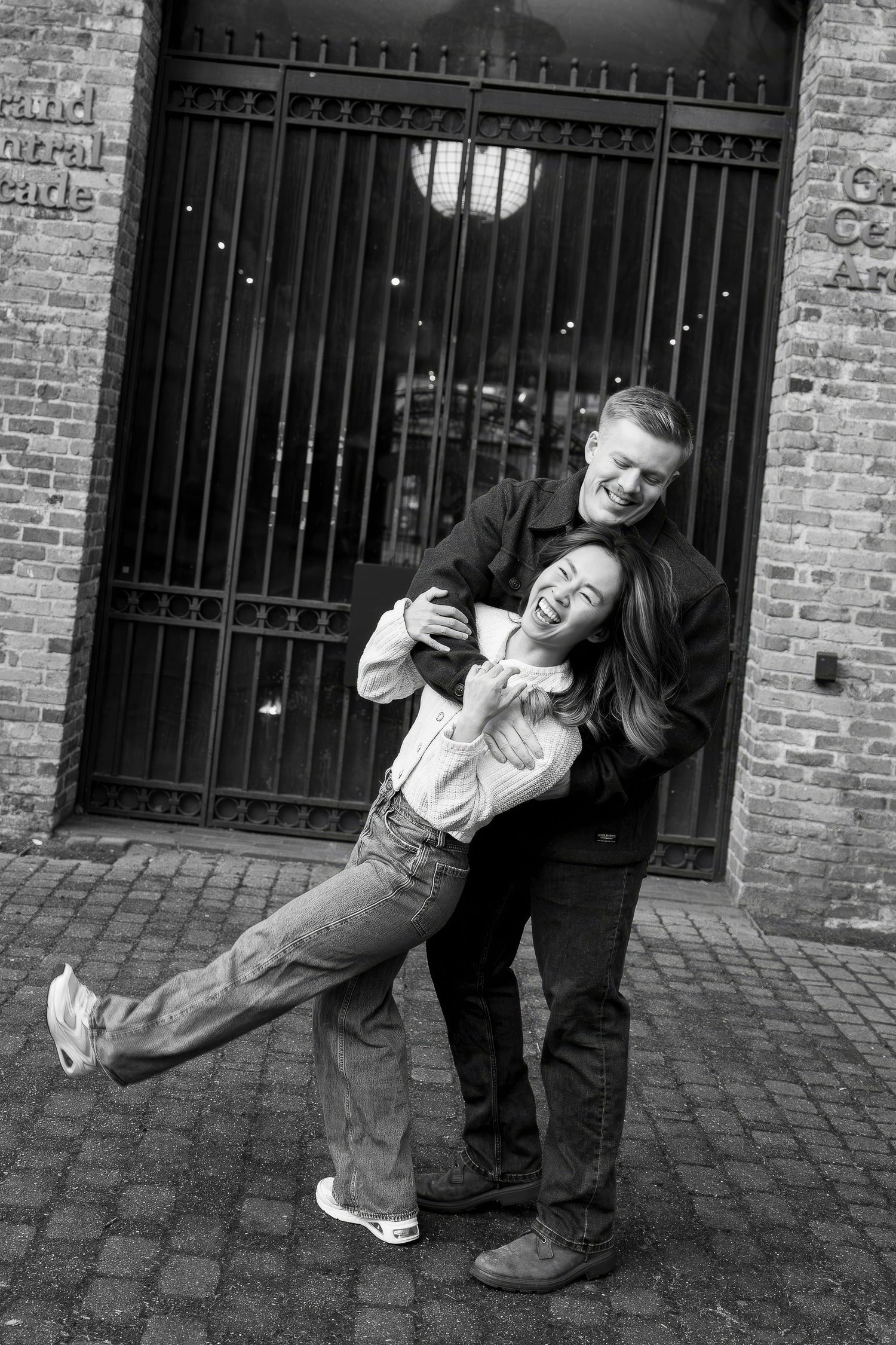 A sequence of black and white photos showing playful interaction between two people against a brick wall with iron bars.