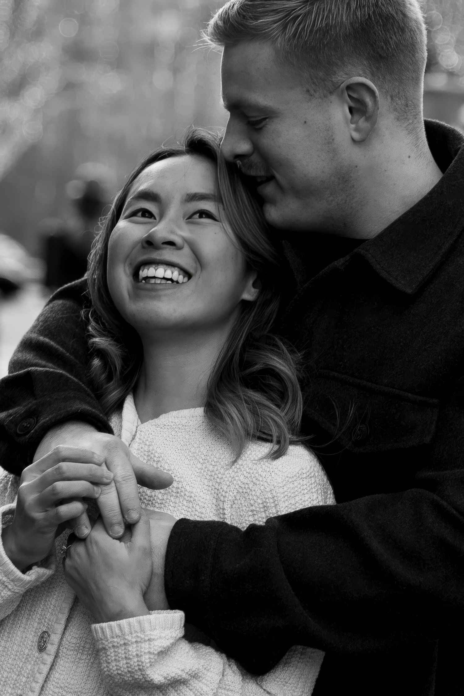 A couple shares an intimate black and white moment together, laughing and embracing in matching sweaters.
