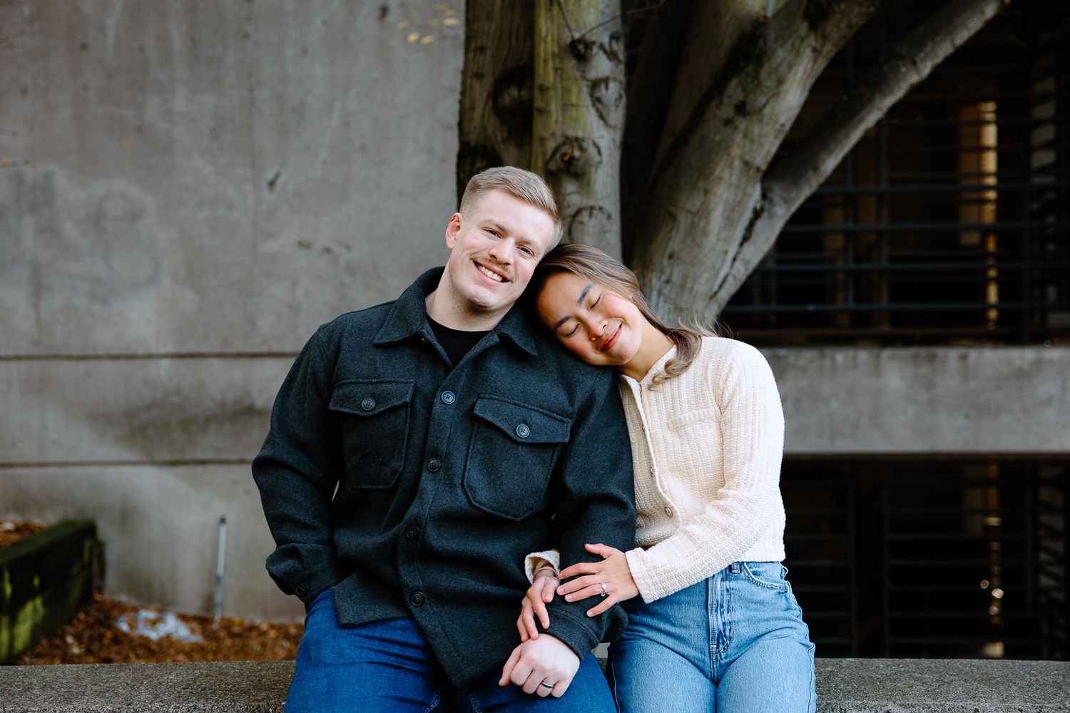 A couple sitting and posing together on concrete steps in casual attire.