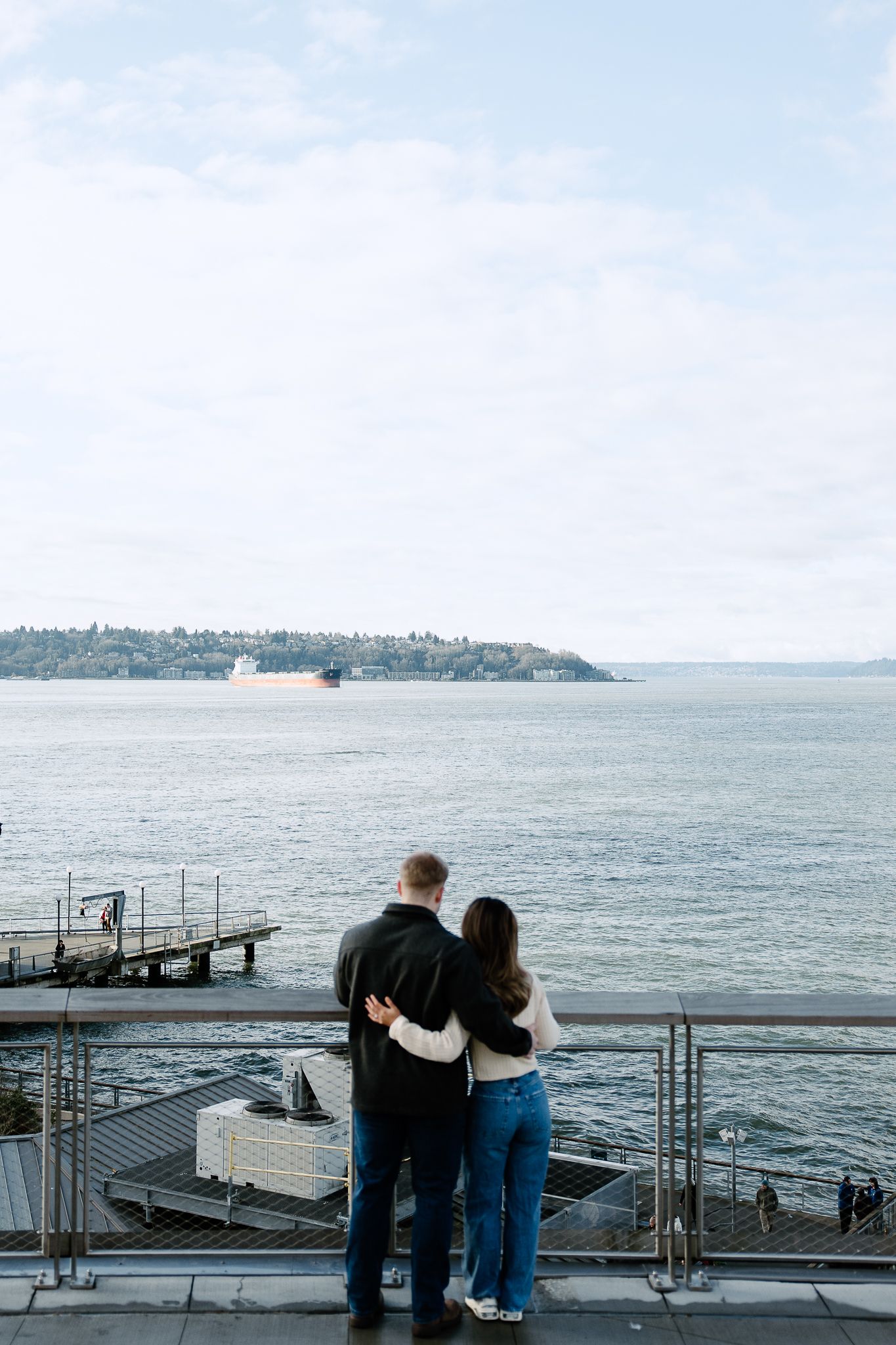 A couple stands together overlooking a waterfront pier and harbor view.