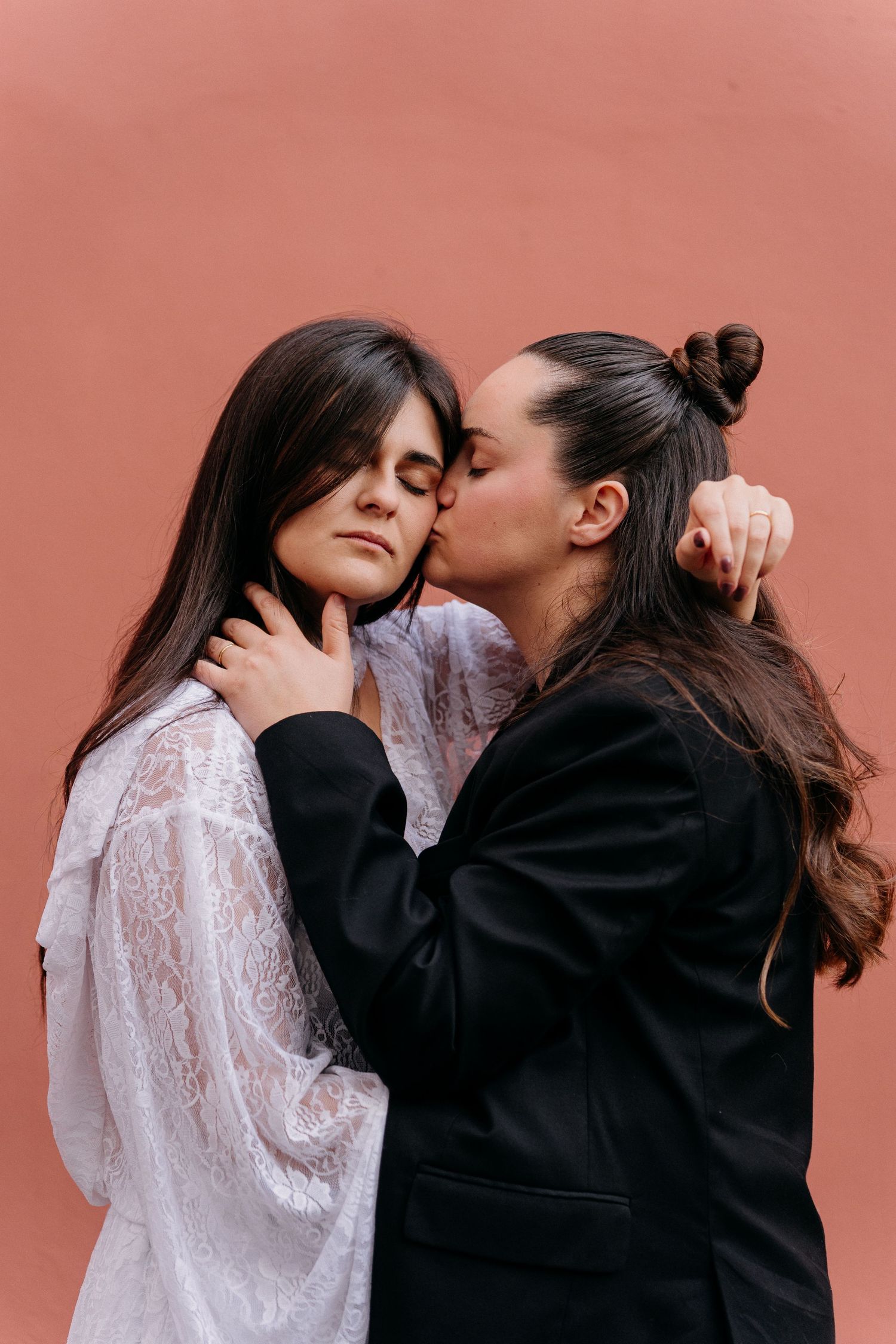 A couple in contrasting black and white outfits share intimate moments in a progressive sequence against a pink wall.