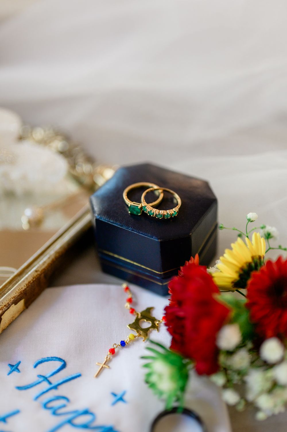 Wedding details including gold rings, red flowers, and handwritten notes on a light colored surface.