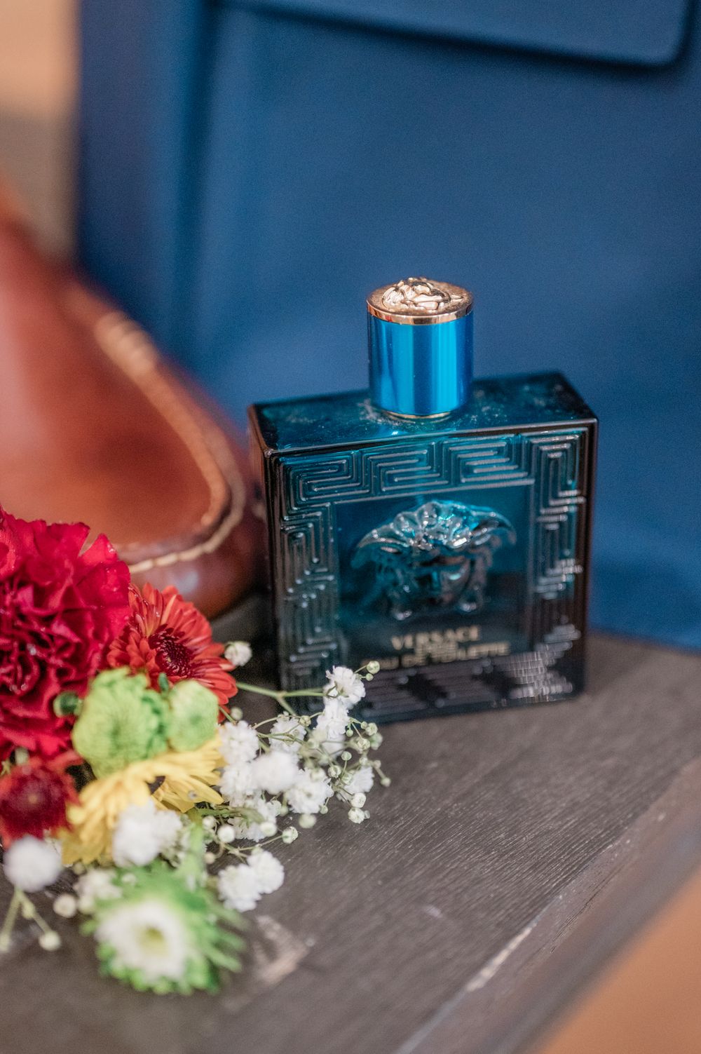 Wedding details featuring a blue Versace perfume bottle with engagement ring and colorful floral accents.