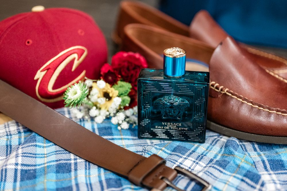 Wedding accessories including red cap, blue cologne, brown leather shoes and plaid fabric.