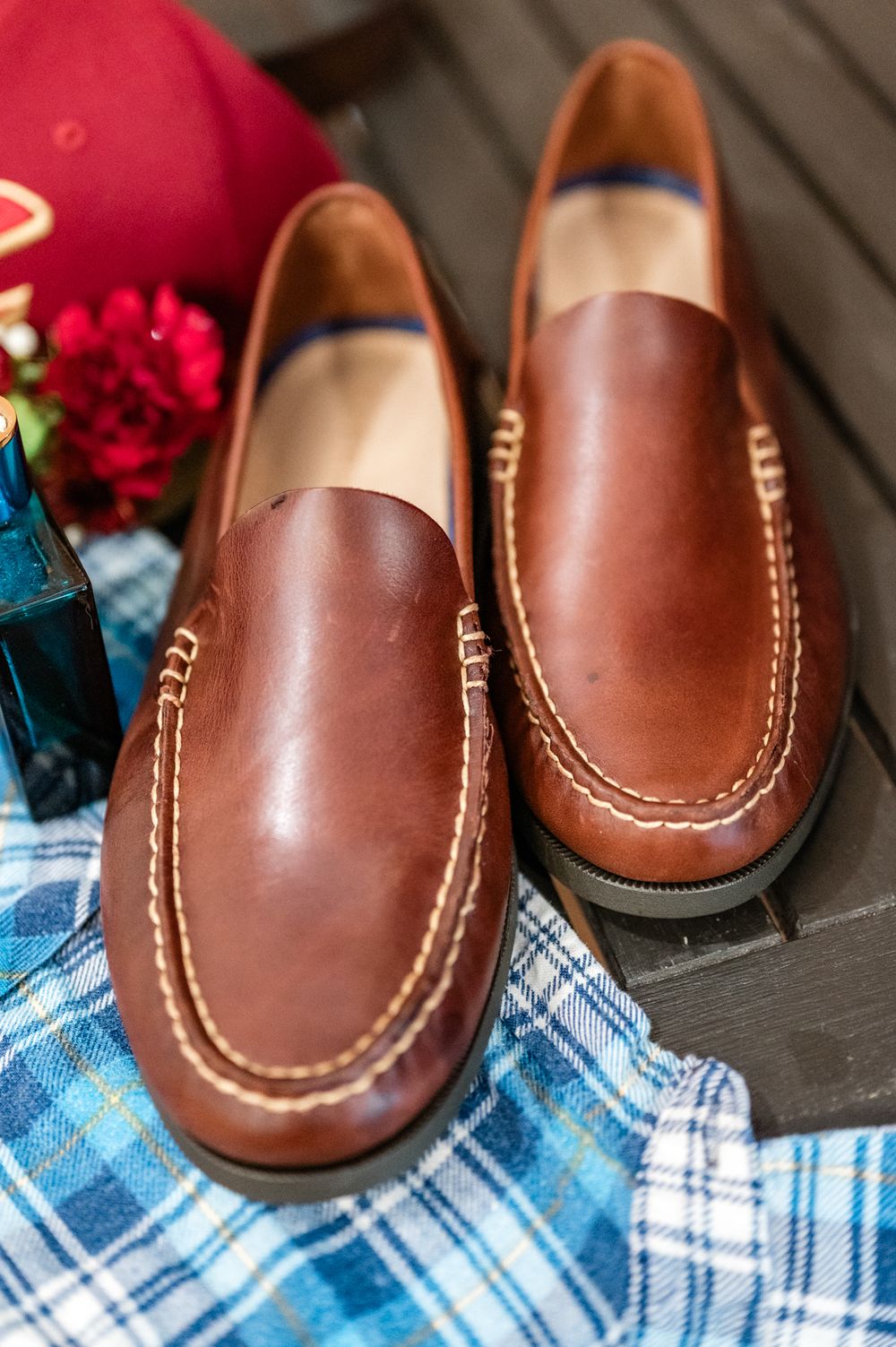 Close-up view of brown leather loafers with white stitching on blue plaid fabric.