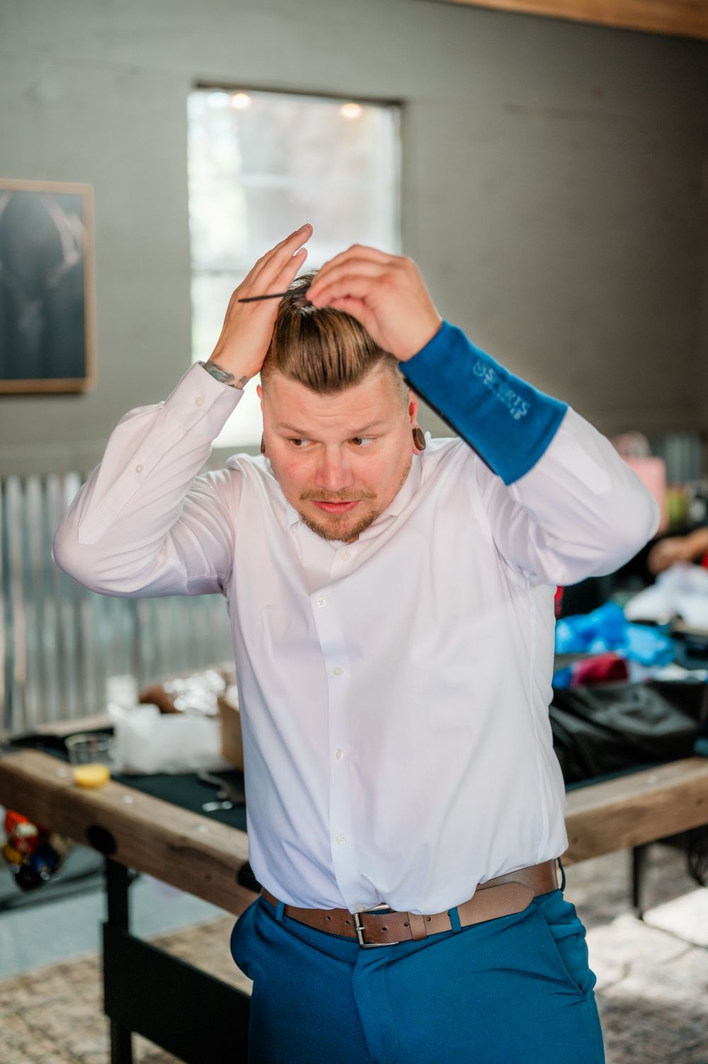 A person in a white dress shirt and blue pants adjusts their hair while getting ready for a formal event.