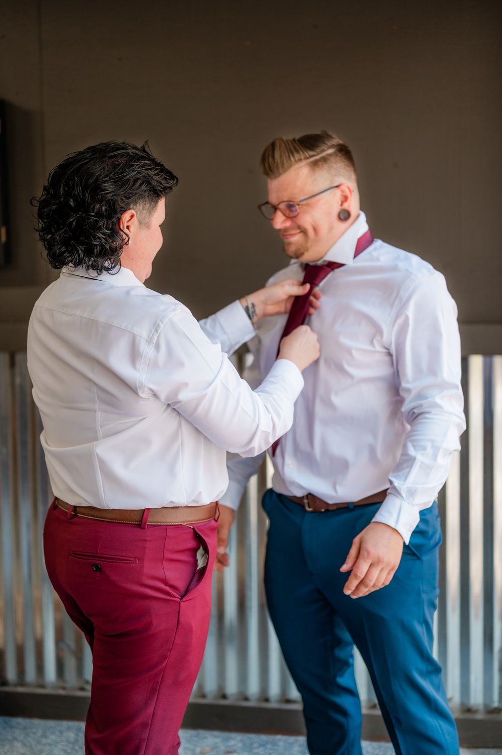 Two people in formal attire help each other with wardrobe adjustments before an event.