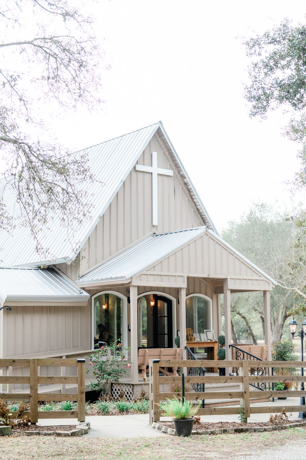 Rustic farmhouse style wedding venue with white wooden buildings and split rail fencing surrounded by trees.