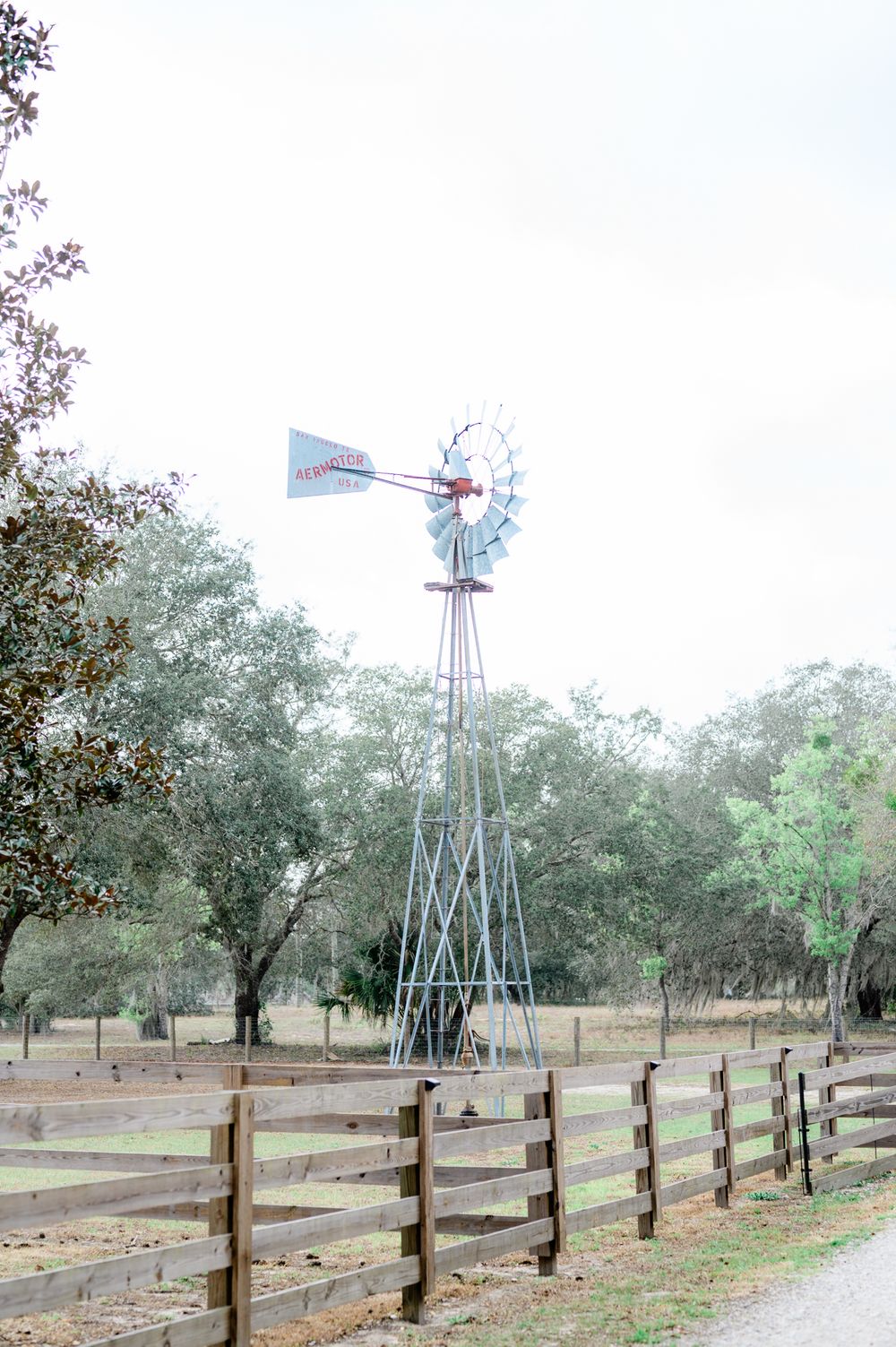 Rustic windmill stands tall against cloudy sky with wooden fence in foreground.