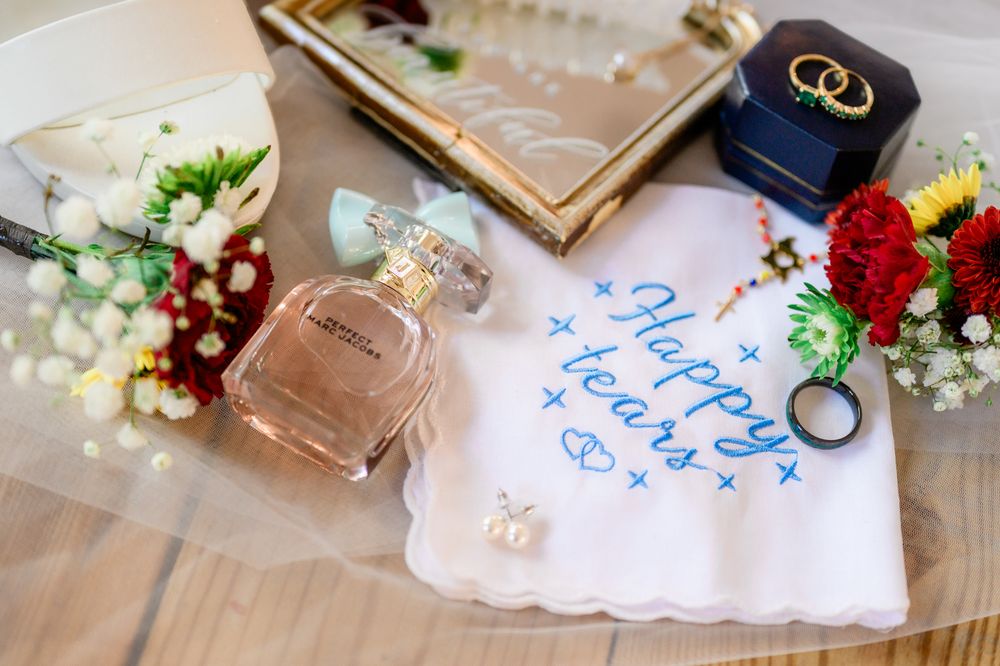 Wedding details including rings, handkerchiefs and floral arrangements on a light surface.