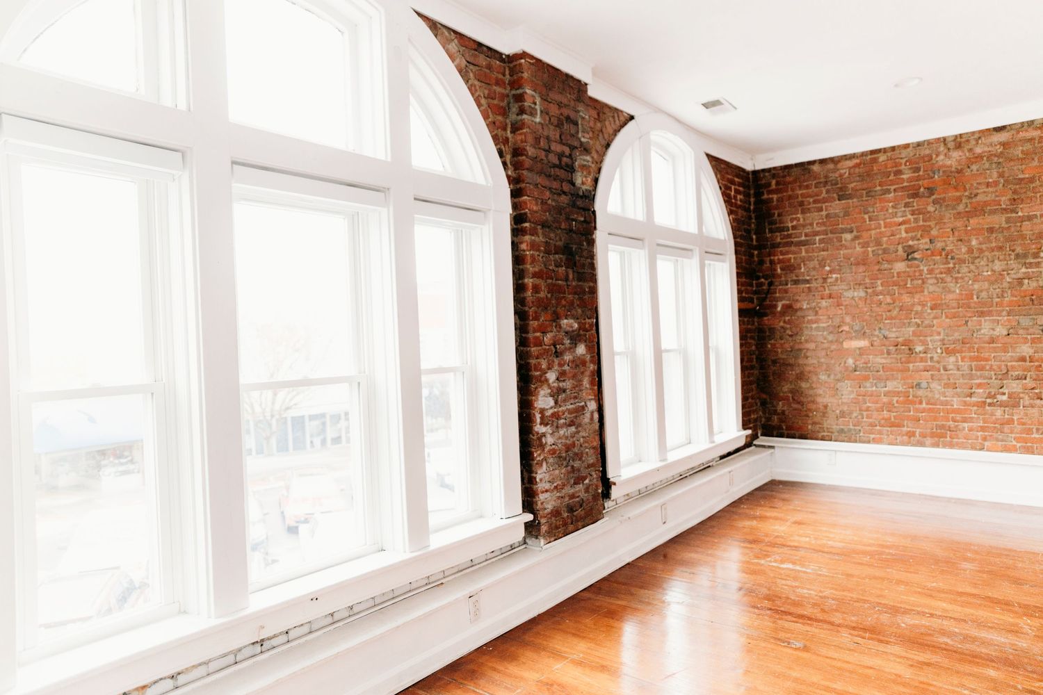Empty loft apartment interior with exposed brick walls, hardwood floors, and large windows letting in natural light.