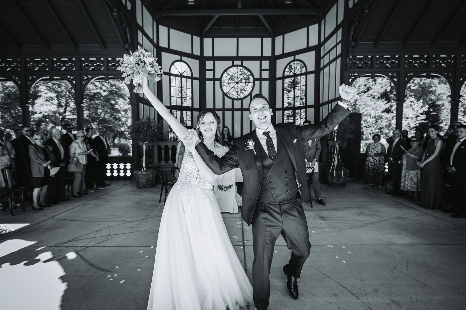 A couple in wedding attire poses in front of green foliage on their special day.