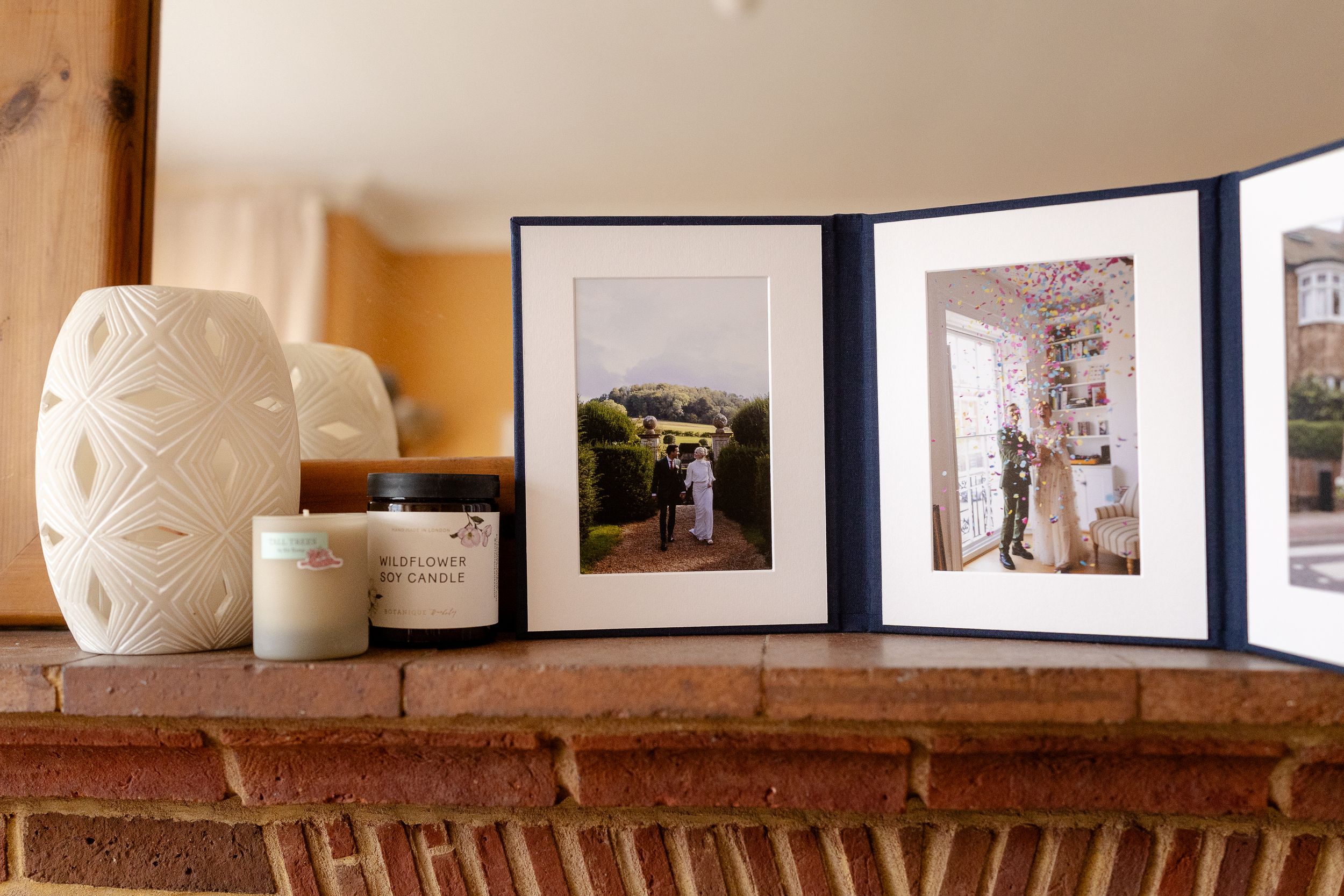 A rustic wooden shelf displays framed photographs and white ceramic vases against a warm-toned wall.