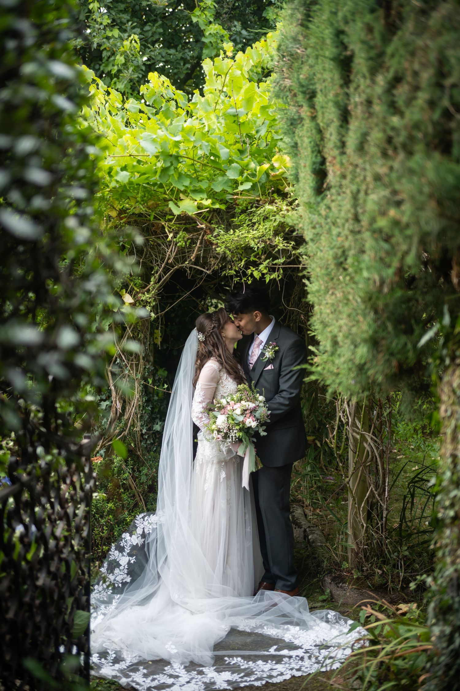 Wedding guests throw colorful confetti at a couple outside a rustic stone building during a celebration.