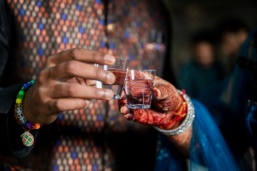 Close-up shot of hands holding small glasses during a toast at a festive gathering with colorful lights in background.