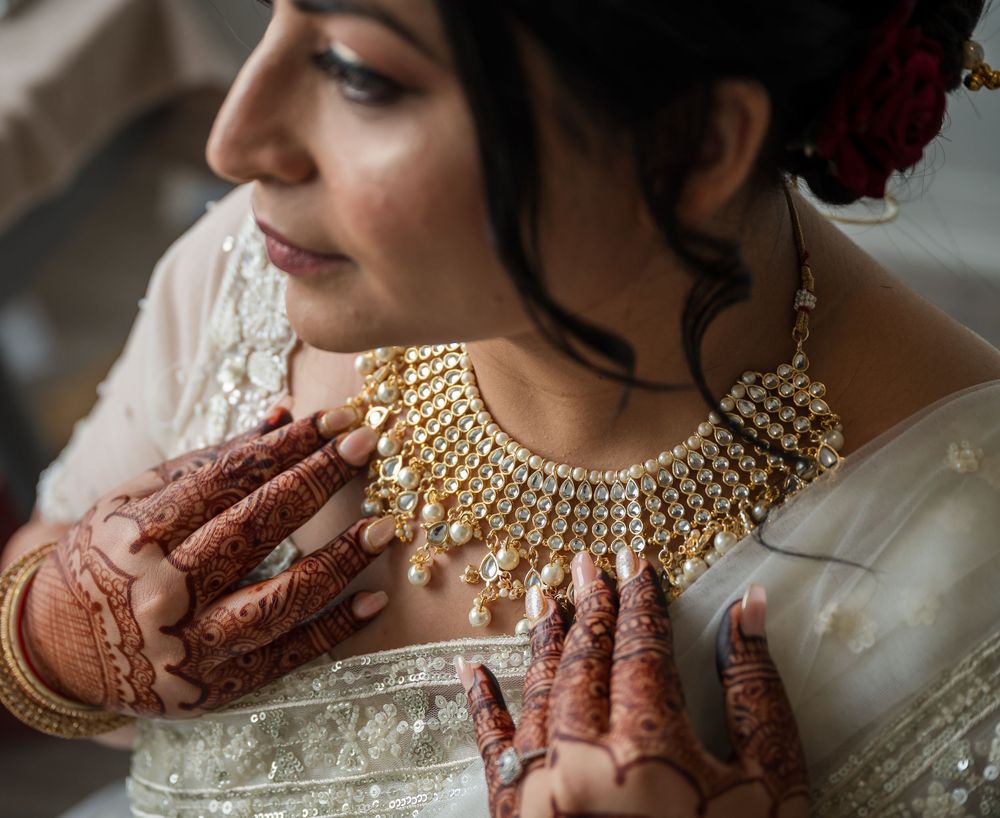 Close-up of traditional Indian bridal jewelry and henna adorned hands adjusting an ornate gold necklace.