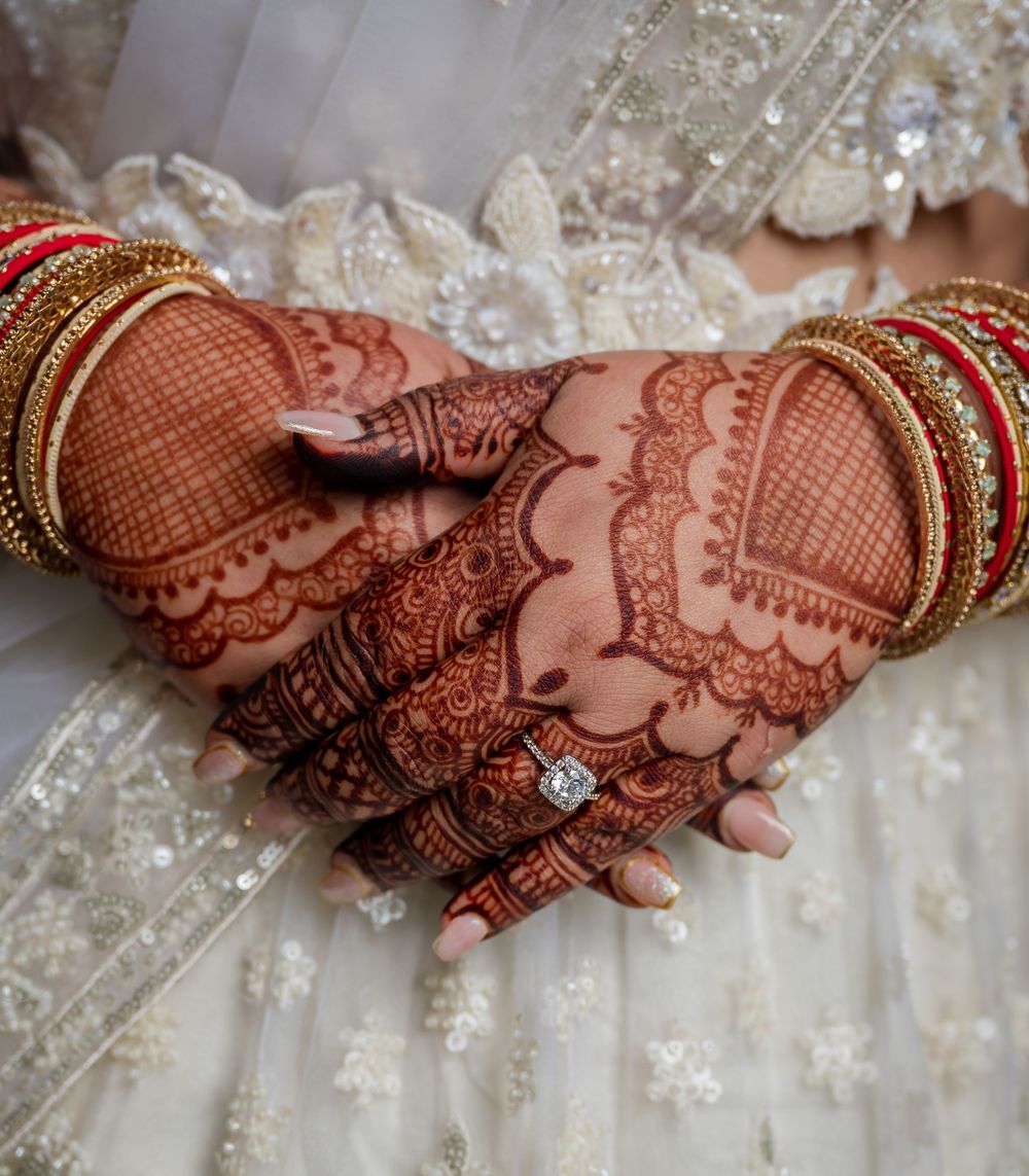 Detailed henna mehndi designs adorn hands resting on white embroidered fabric with traditional Indian bridal jewelry.