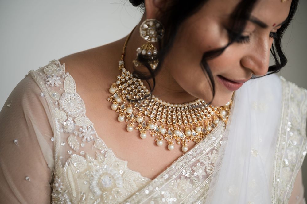 Close-up of ornate gold and pearl Indian bridal necklace and earrings with white lace and fabric details.