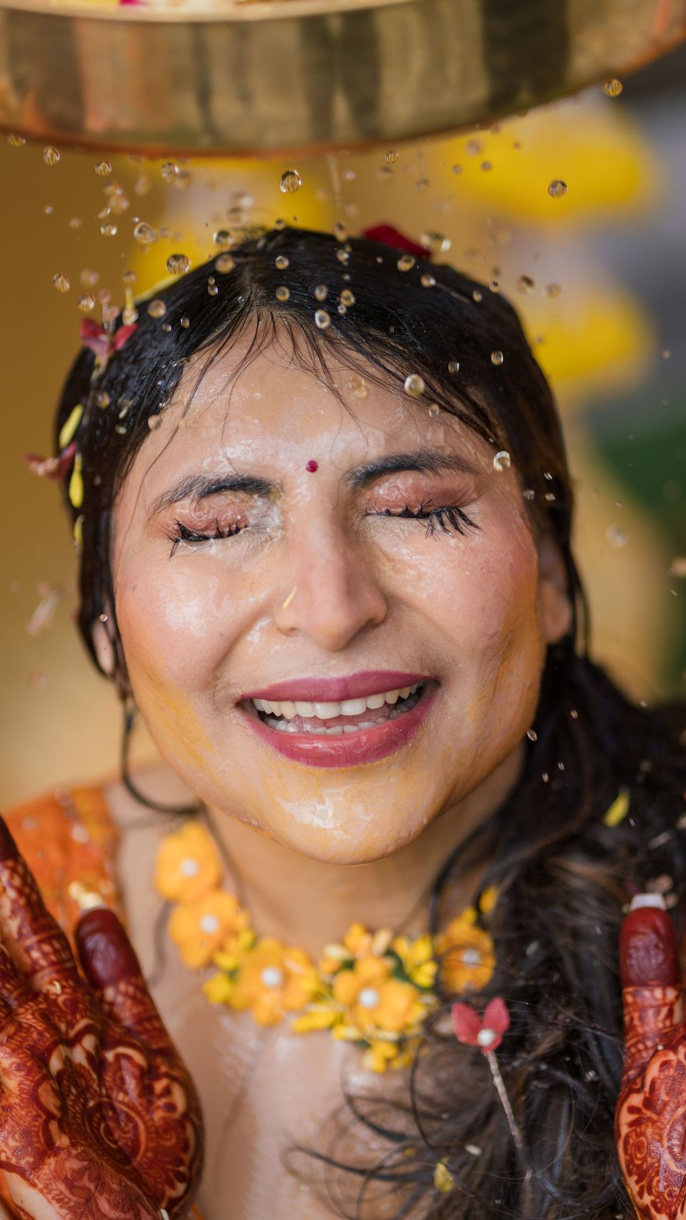 A smiling person in traditional Indian attire with mehndi and bindi during a celebratory moment with falling glitter.