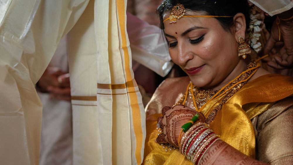 Traditional Indian bride wearing gold silk saree and ornate jewelry looks down with closed eyes during wedding ceremony.